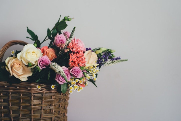 Assortment of different colored spring flowers in a basket with grey backdrop.