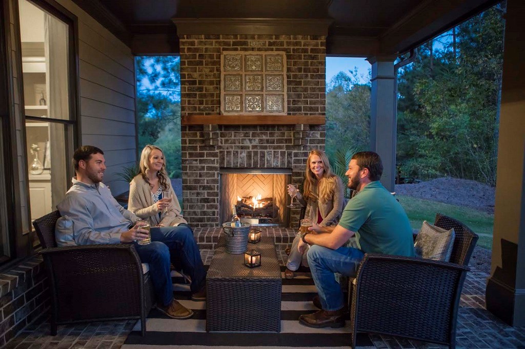 Two couples sitting on the covered back porch by a fire.