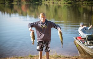 Boy holding up fish in front of Lake Sterling