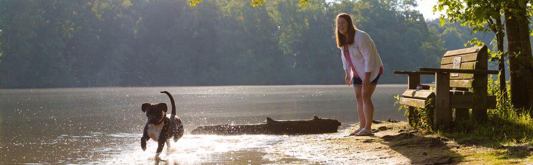 A woman and her dog playing catch by Lake Sterling